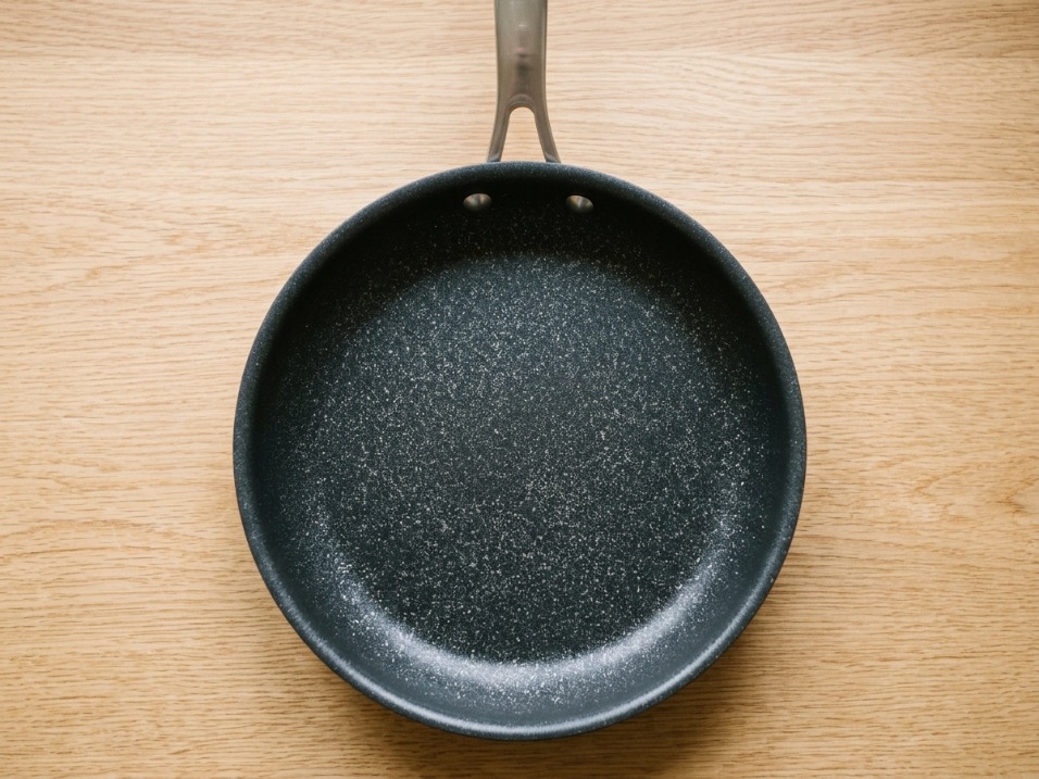 Overhead view of a hard-anodized frying pan with a speckled ceramic nonstick coating and riveted stainless handle