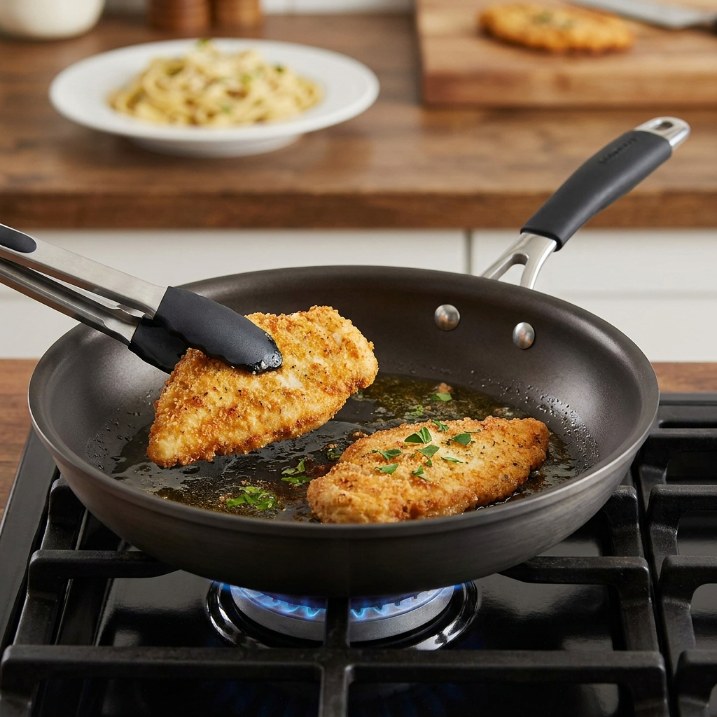 Dark charcoal nonstick frying pan on gas stove with golden breaded chicken lifted by tongs