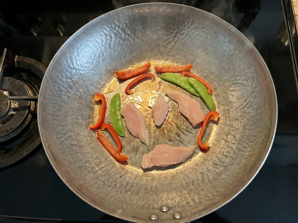 Carbon steel wok on a cooktop with scattered stir fry ingredients showing proper spacing