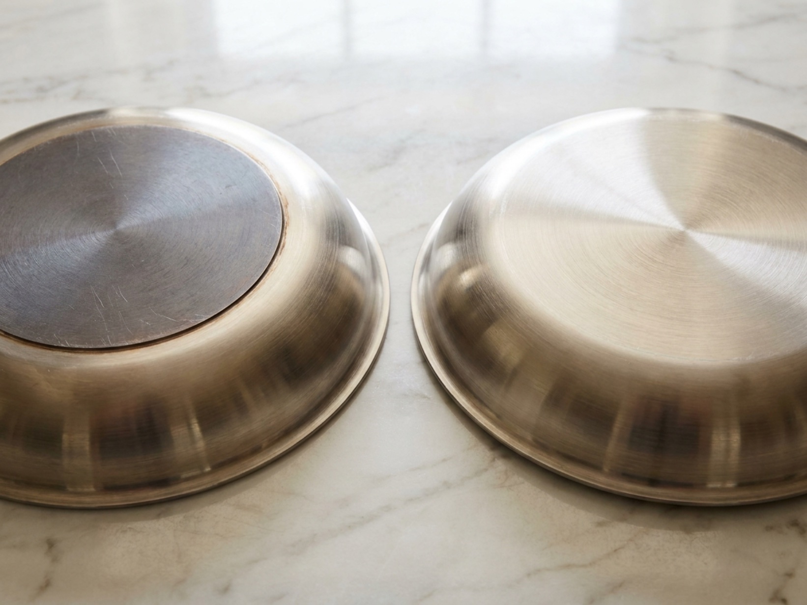 Two pans flipped upside-down showing disc-bottom construction versus fully-clad uniform base