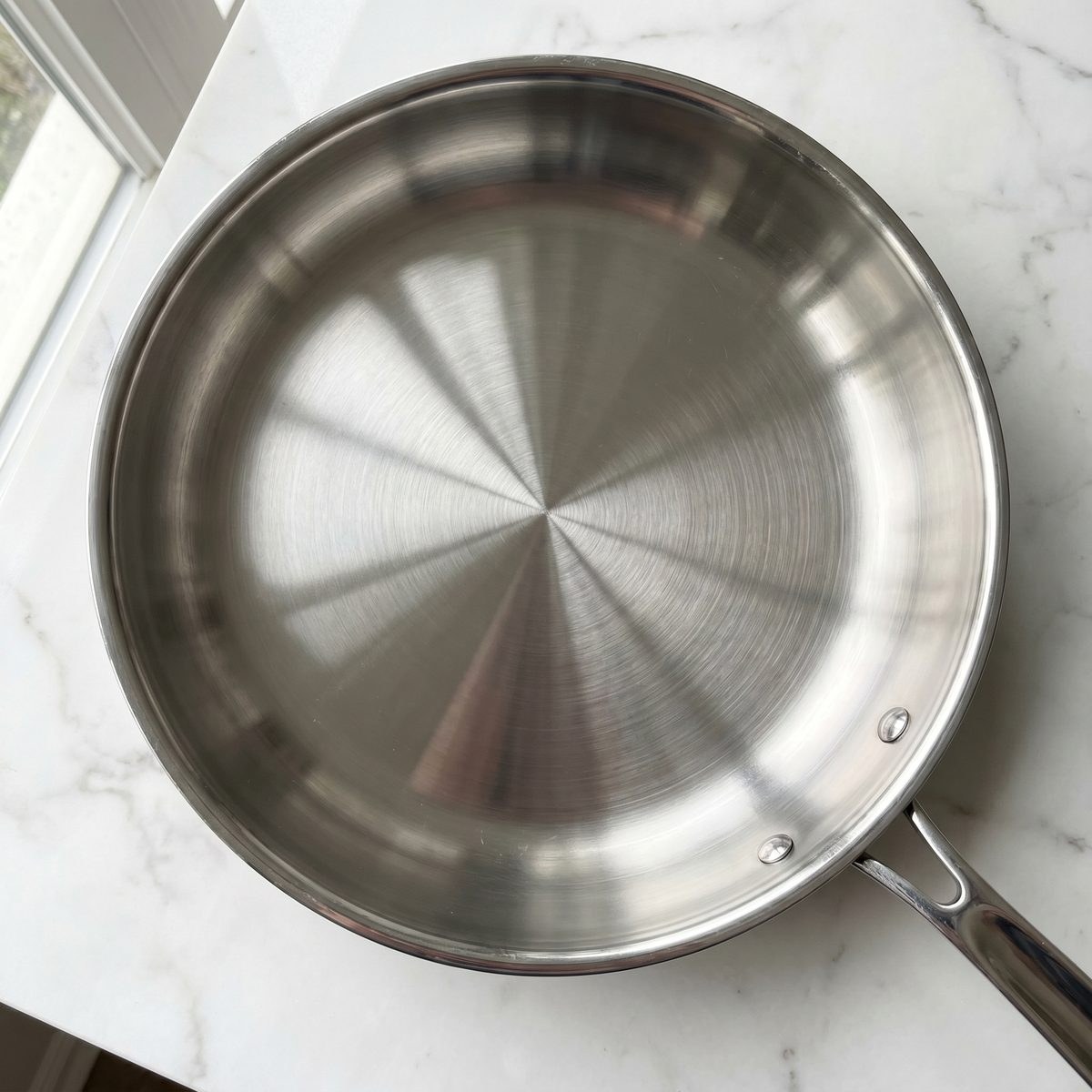Stainless steel frying pan fully restored to a clean mirror-polished surface after cleaning a severe burn