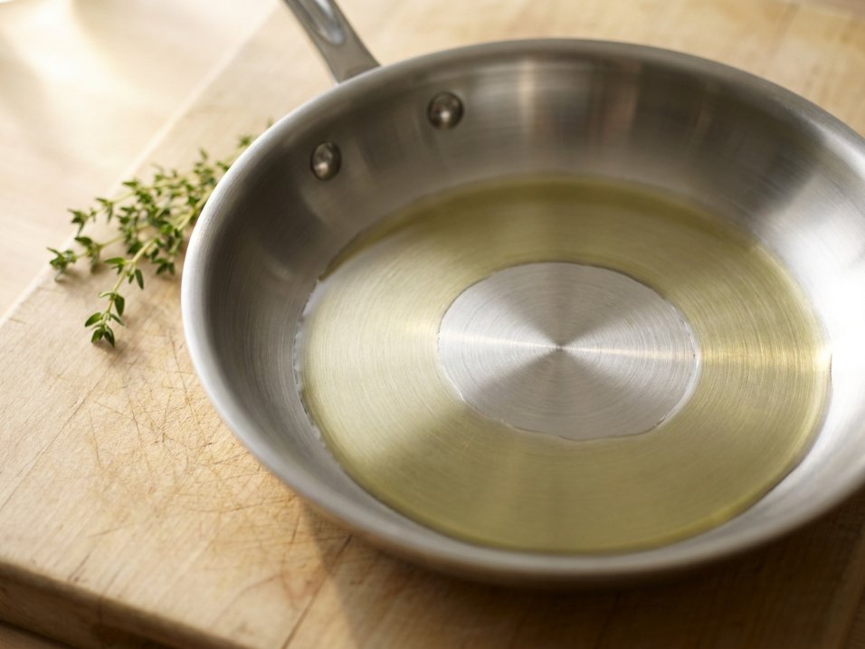 Interior of a stainless steel skillet showing the smooth cooking surface with golden oil shimmer
