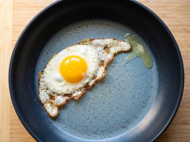 Fried egg with crispy edges sliding freely on a blue-grey speckled ceramic nonstick cooking surface