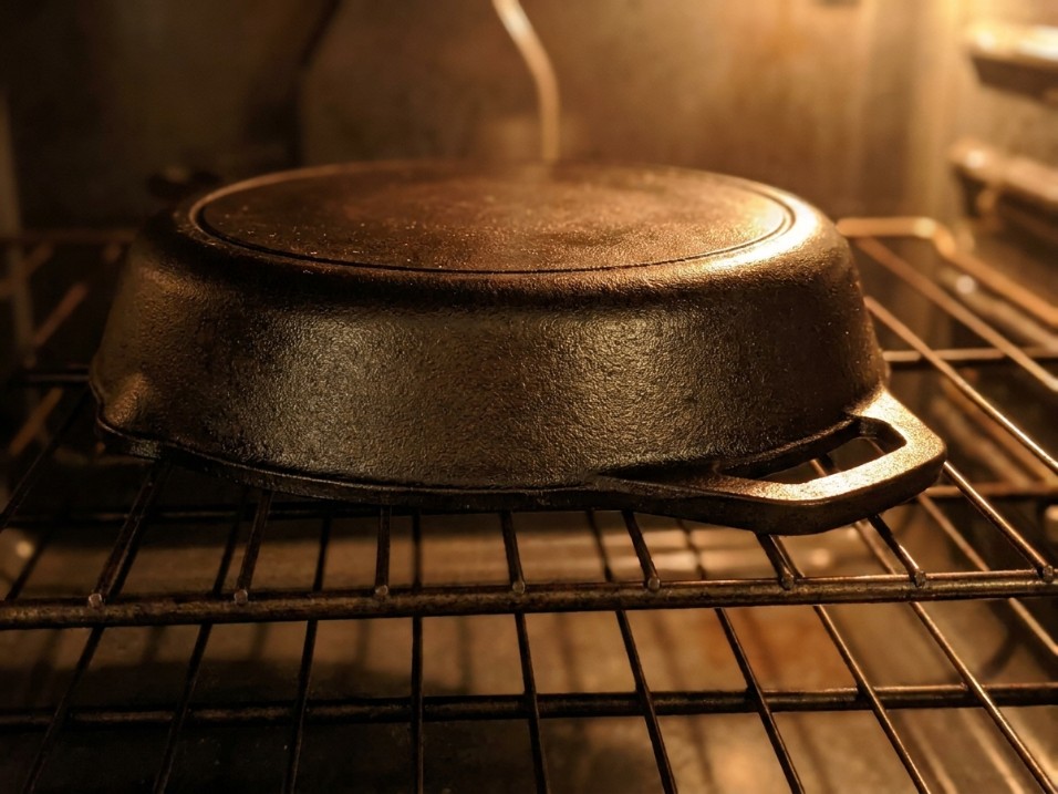 Cast iron skillet turned upside down on an oven rack with a thin oil sheen, warm interior oven light