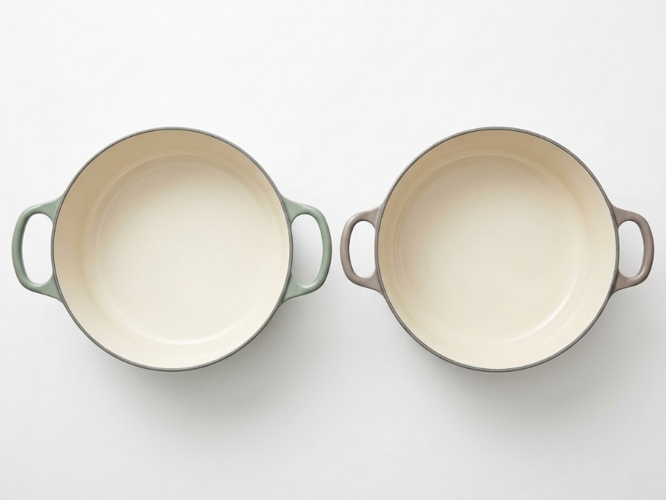 Two enameled cast iron dutch ovens with lids off, showing interior color and the different widths of their handle openings