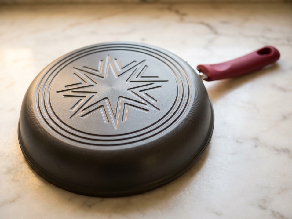 Bottom of hard anodized nonstick pan showing star-shaped heat distribution pattern with concentric rings on marble surface
